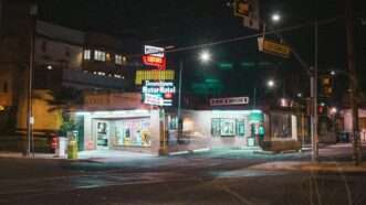 A street-corner liquor store lit up at night. | Photo by <a href=%40linginite0f4.html Ling</a> on <a href=white-and-red-store-front-during-night-time-ioe1-sfnitc9678.html