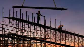 A factory under construction, with a beam being lowered and a crew member standing ready. | Somnuek Saelim | Dreamstime.com