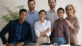 A happy and diverse group of people in a business environment: six people of different ages, races, and genders. | Fizkes | Dreamstime.com