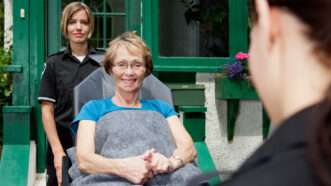 Paramedics wheel out an elderly woman, who is sitting up and smiling, on a gurney. | Tyler Olson | Dreamstime.com