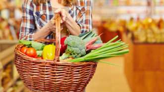 Woman in a supermarket carrying a basket full of fresh produce. | Robert Kneschke | Dreamstime.com