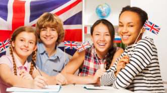 Happy teens in a classroom hold U.K. "Union Jack" flags. | Sergey Novikov | Dreamstime.com