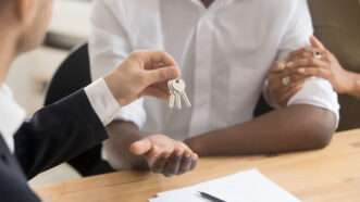 A man hands a couple a key to their new home | Photo 140714356 © Fizkes | Dreamstime.com