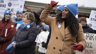 Stacy Davis Gates in a winter coat with her fist raised, standing next to Randi Weingarten | E. Jason Wambsgans/TNS/Newscom