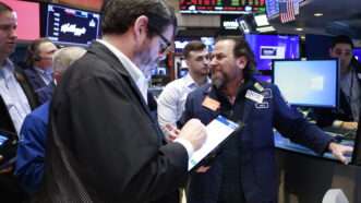 A group of Wall Street traders huddle around a desk at the New York Stock Exchange. | John Angelillo/UPI/Newscom